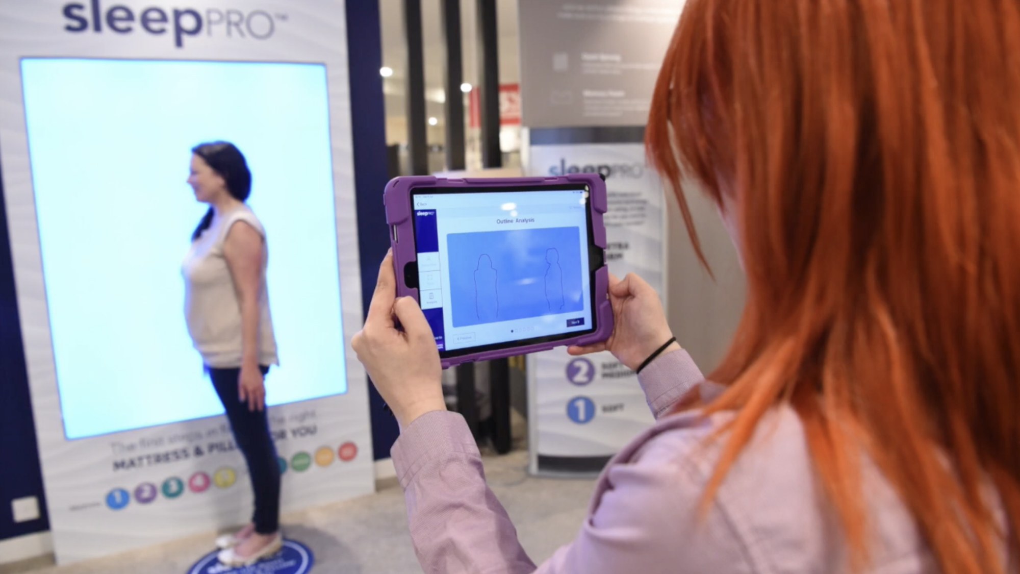 A colleague running the Sleep Pro body-shape scan in store on an iPad, with an outline analysis screen shown